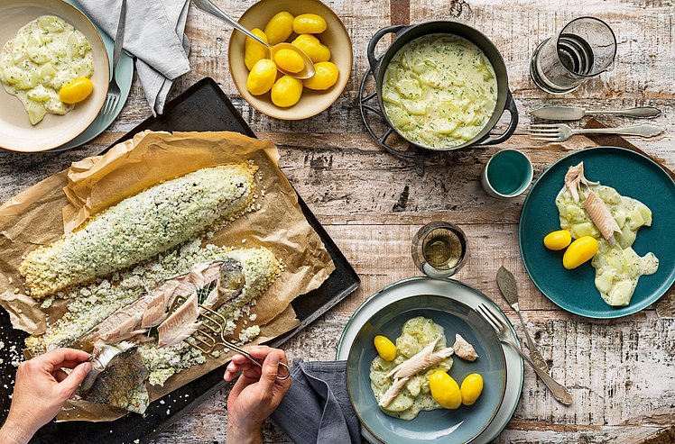 Blick auf einen gedeckten Tisch mit Fisch und Kartoffeln.