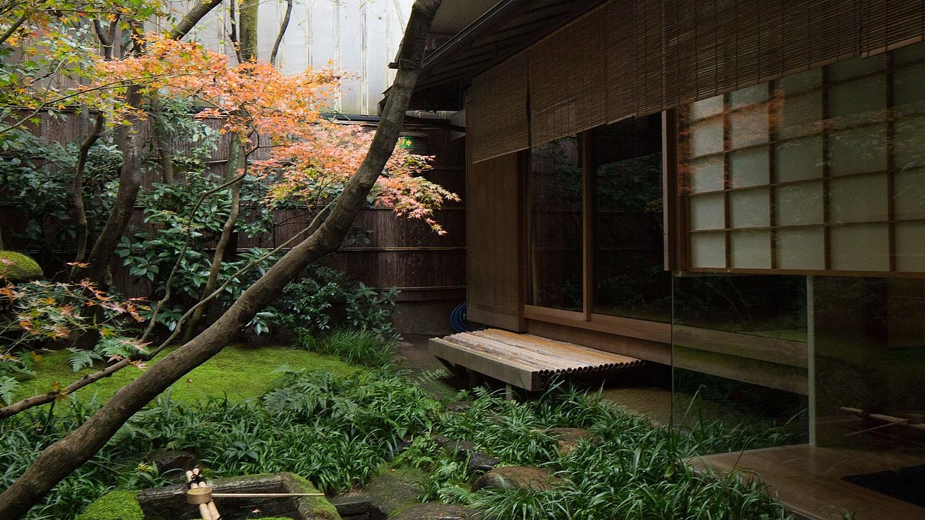 Blick vom zentralen Lichthof auf eine Treppenstufe vor der geöffneten Schiebetür, die in das Tawaraya Ryokan führt